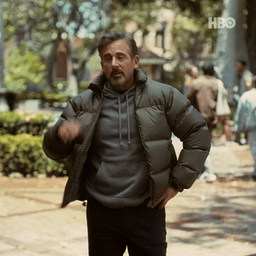 A Man In A Padded Jacket Is Standing On A Sidewalk In Front Of A Sign That Says Hbo GIF