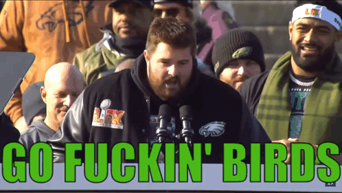 A Man In A Philadelphia Eagles Shirt Stands In Front Of A Microphone With The Words Go Fuckin Birds Above Him GIF