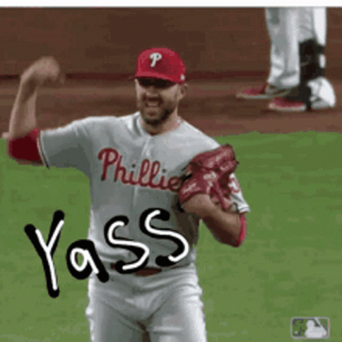 A Man In A Phillies Jersey Is Flexing His Muscles On A Baseball Field GIF