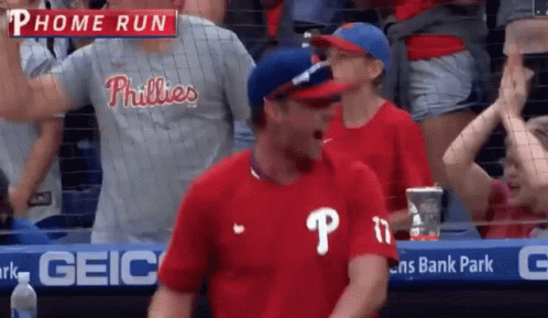 A Man In A Phillies Shirt Is Standing In The Stands GIF