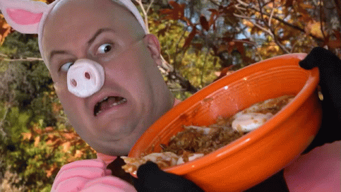 A Man In A Pig Costume Is Holding An Orange Bowl Of Food GIF