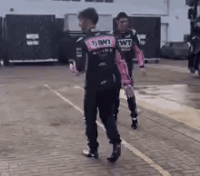 a man in a pink and black racing suit is walking down a sidewalk .