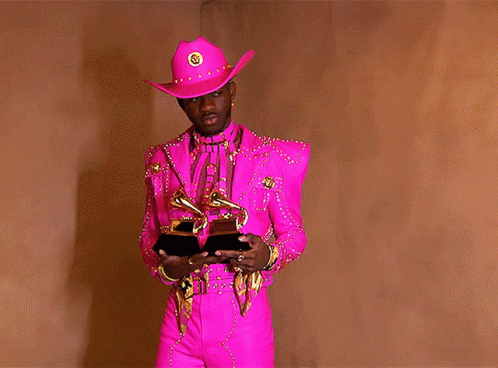 A Man In A Pink Cowboy Hat Is Holding A Pair Of Grammys GIF
