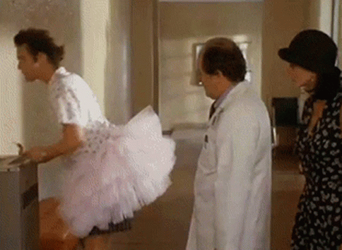 A Man In A Pink Dress Is Standing Next To A Doctor And A Woman In A Hat . GIF