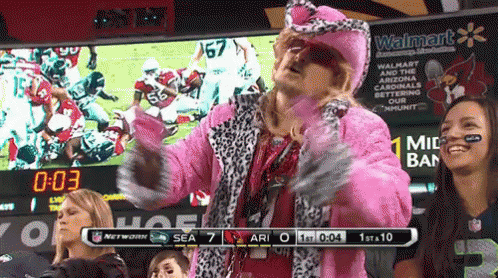 A Man In A Pink Fur Coat Stands In Front Of A Scoreboard That Says Walmart GIF