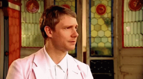 A Man In A Pink Jacket And White Shirt Is Standing In Front Of A Stained Glass Door . GIF