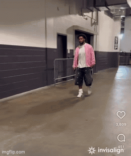 A Man In A Pink Jacket Is Walking Down A Hallway With Invisalign GIF