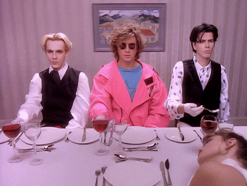 A Man In A Pink Jacket Sits At A Table With Plates And Glasses Of Wine GIF