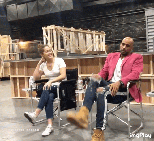 A Man In A Pink Jacket Sits Next To A Woman In A Chair GIF