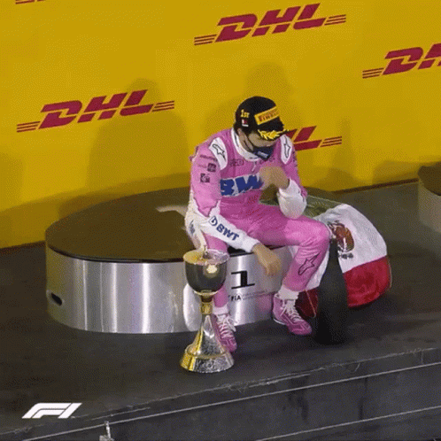 A Man In A Pink Racing Suit Is Sitting On A Podium With A Trophy In Front Of A Dhl Sign GIF