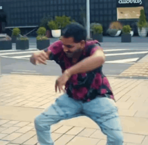 A Man In A Pink Shirt And Blue Jeans Is Dancing On A Brick Sidewalk . GIF