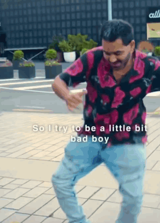 A Man In A Pink Shirt And Blue Jeans Is Dancing On A Brick Sidewalk . GIF