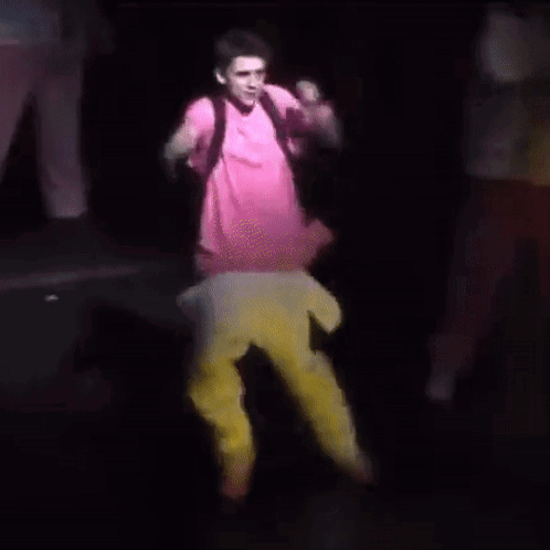 A Man In A Pink Shirt And Yellow Pants Is Dancing On Stage . GIF