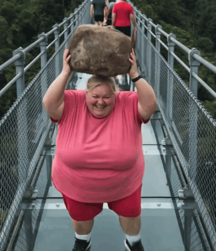 A Man In A Pink Shirt Is Carrying A Large Rock Over His Head GIF