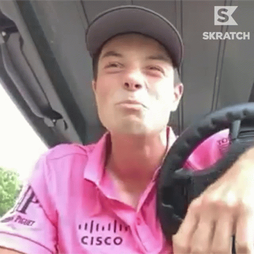 a man in a pink shirt is driving a golf cart .