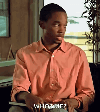 A Man In A Pink Shirt Is Holding A Book And Asking Who Me ? GIF