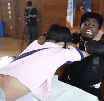 A Man In A Pink Shirt Is Hugging Another Man In A Black Hat GIF