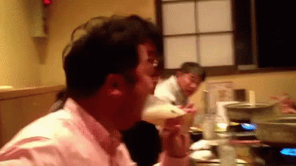 A Man In A Pink Shirt Is Sitting At A Table Drinking A Beer . GIF