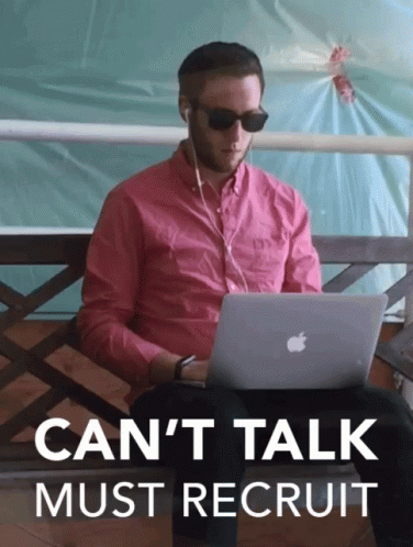 A Man In A Pink Shirt Is Sitting On A Bench Using An Apple Laptop With The Words " Can 'T Talk Must Recruit " Above Him GIF