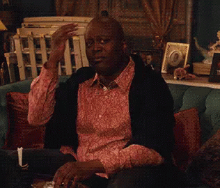 A Man In A Pink Shirt Is Sitting On A Couch Drinking A Glass Of Wine . GIF