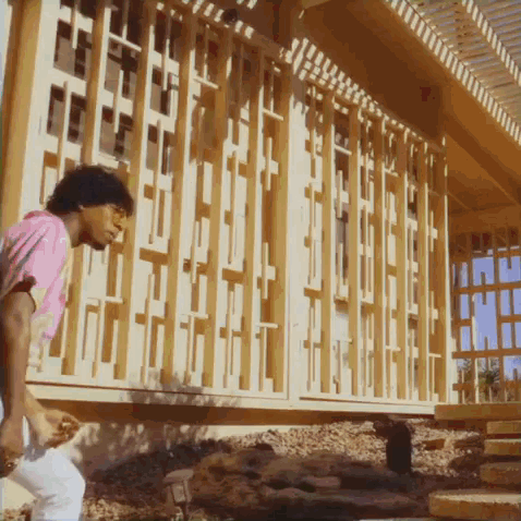 A Man In A Pink Shirt Is Standing In Front Of A Building That Is Being Built GIF