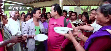 A Man In A Pink Shirt Is Standing In Front Of A Crowd Of People Holding Plates . GIF