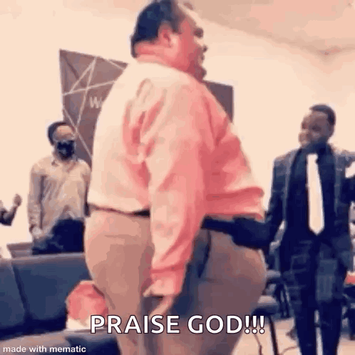 A Man In A Pink Shirt Is Standing In Front Of A Group Of People In A Church And Praising God . GIF
