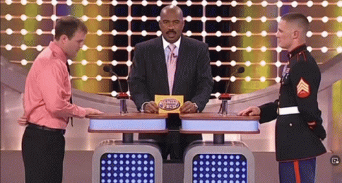 A Man In A Pink Shirt Is Standing Next To A Man In A Military Uniform On A Game Show Called Family Feud GIF