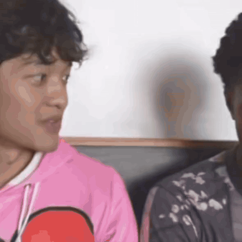 A Man In A Pink Shirt Is Talking To Another Man In A Black Jacket . GIF