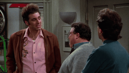 A Man In A Pink Shirt Is Talking To Two Other Men In A Room GIF