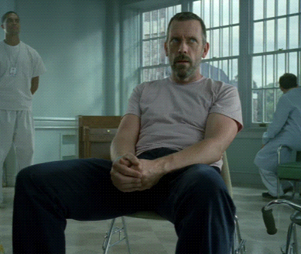 A Man In A Pink Shirt Sits In A Chair With His Hands Folded GIF