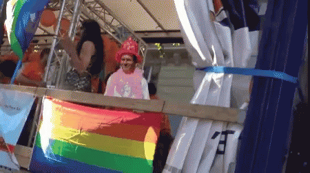 A Man In A Pink Shirt Stands Behind A Rainbow Flag With Chinese Characters On It GIF