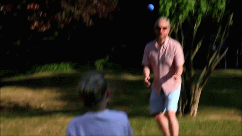 A Man In A Pink Shirt Throws A Golf Ball To Another Man GIF