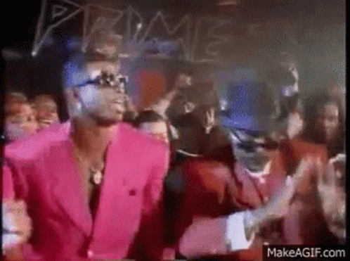A Man In A Pink Suit And A Man In A Red Suit Are Dancing In Front Of A Crowd . GIF