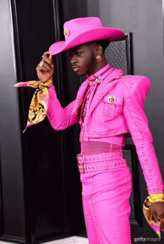A Man In A Pink Suit And Cowboy Hat Is Standing In Front Of A Black Door GIF
