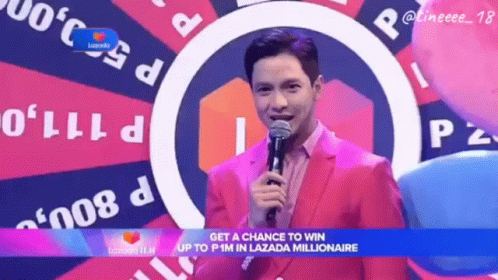 A Man In A Pink Suit Holds A Microphone In Front Of A Lazada Logo GIF