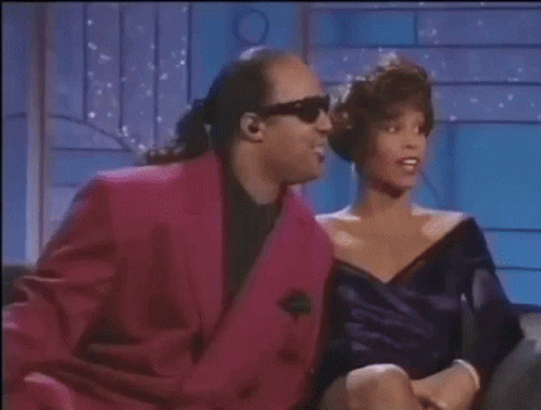 A Man In A Pink Suit Is Sitting Next To A Woman In A Purple Dress On A Couch . GIF