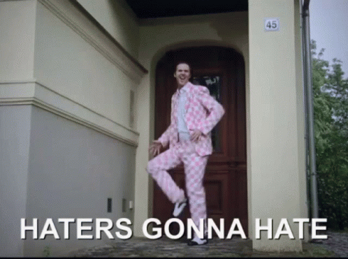 A Man In A Pink Suit Is Standing In Front Of A Door With The Words Haters Gonna Hate Written Below Him GIF