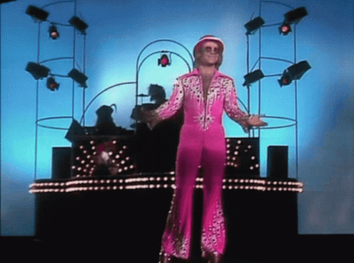 A Man In A Pink Suit Is Standing In Front Of A Stage GIF