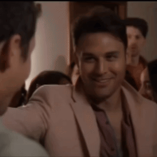 A Man In A Pink Suit Is Talking To Another Man In A Crowd GIF