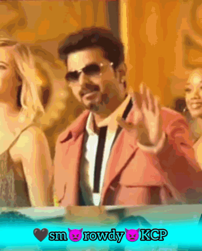 A Man In A Pink Suit Is Waving His Hand In Front Of Two Women GIF