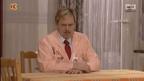 a man in a pink suit sits at a table with a tennis ball on the wall above him that says op12