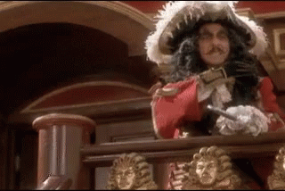 A Man In A Pirate Costume Is Standing On A Balcony With A Sword . GIF