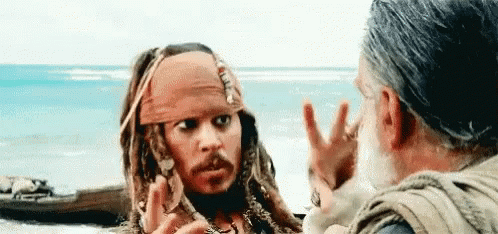 A Man In A Pirate Costume Is Talking To Another Man In Front Of The Ocean . GIF