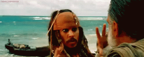 a man in a pirate outfit is talking to another man on the beach .