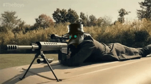A Man In A Plague Doctor Mask Is Laying On The Ground With A Sniper Rifle GIF