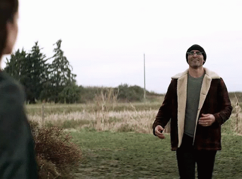 A Man In A Plaid Jacket And A Beanie Is Walking In A Field . GIF