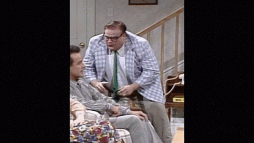A Man In A Plaid Jacket And Tie Is Talking To Another Man In A Chair GIF