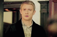 A Man In A Plaid Shirt And A Black Jacket Is Standing In Front Of A Door . GIF