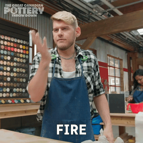 A Man In A Plaid Shirt And Apron Is Making A Fire Gesture GIF